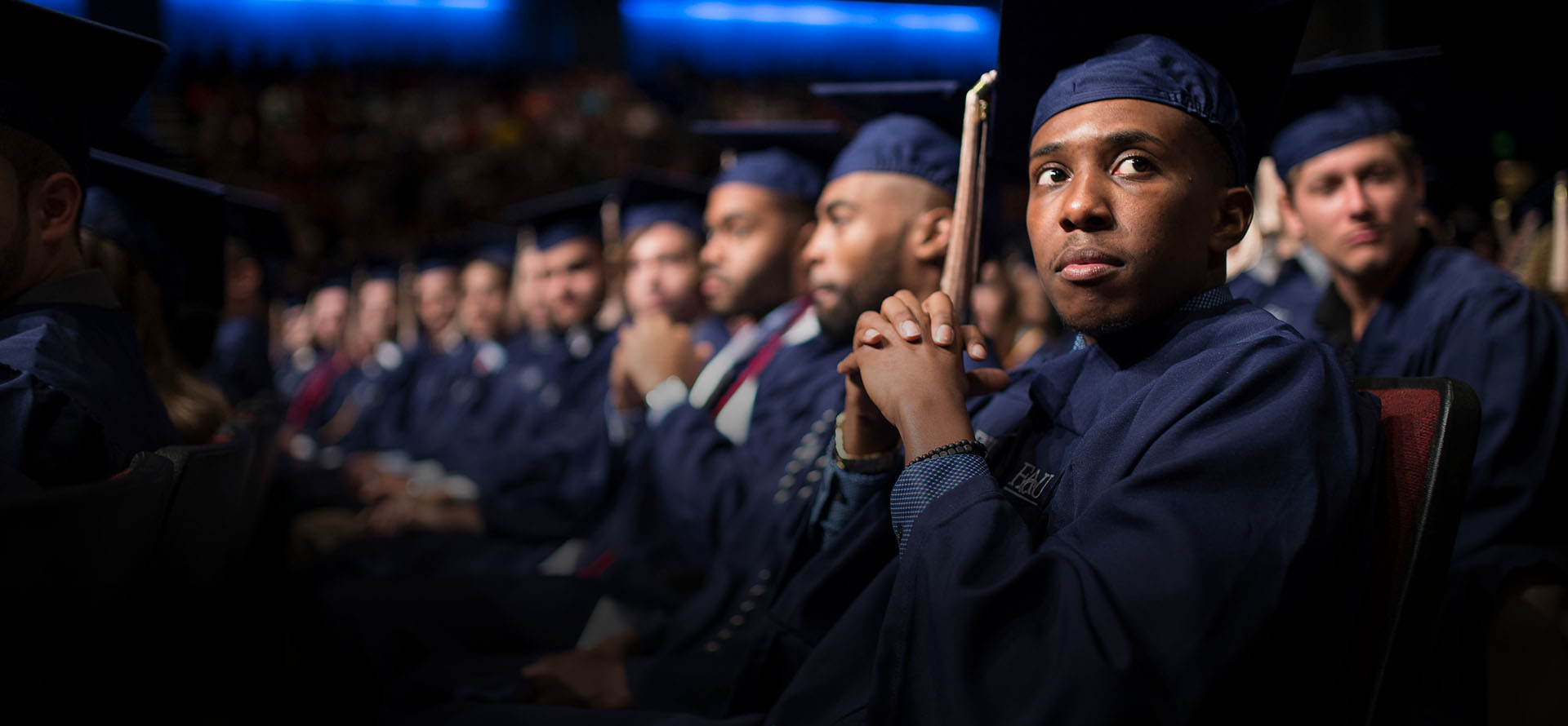 Student in cap and gown sitting down at graduation ceremony